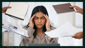 Woman sitting with her hands on her temples surrounded by papers.