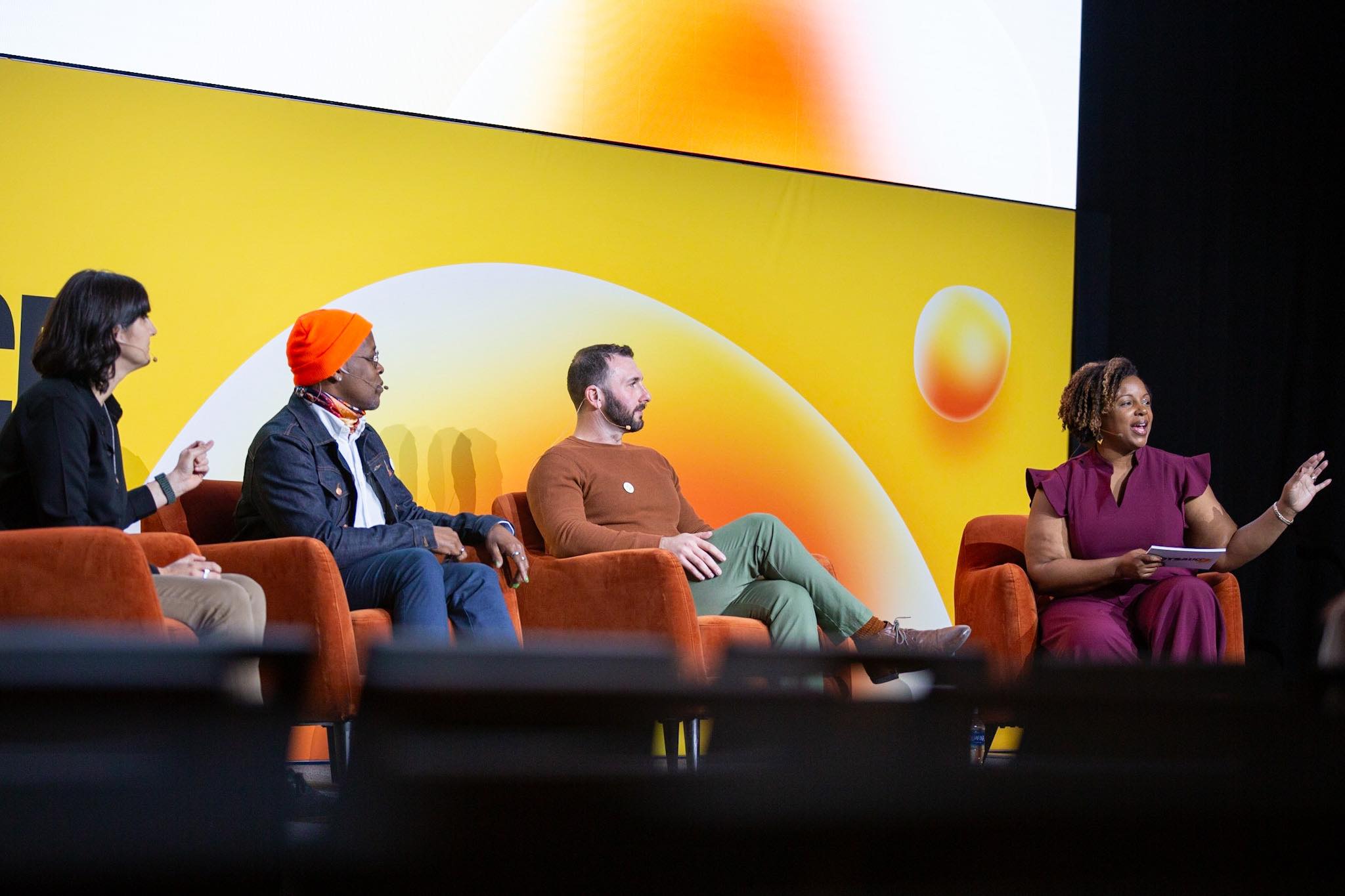Four people with different pronoun preferences and races sitting on the stage discussing the importance of DEI in product development